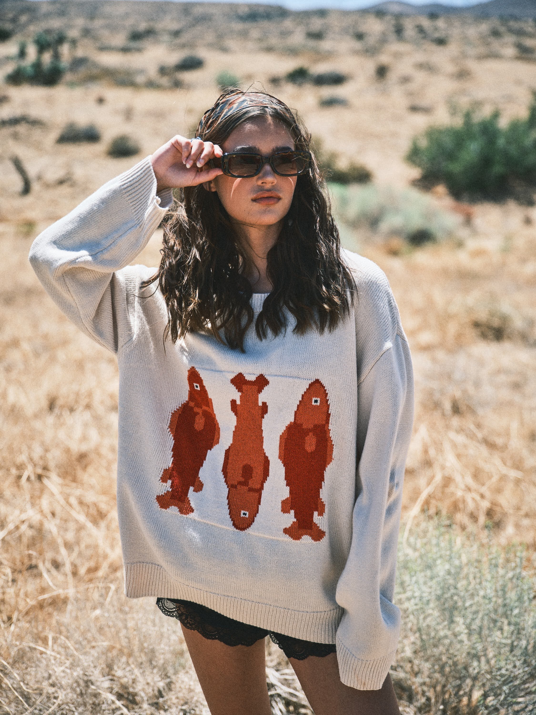 Woman wearing the Marina Fish Knit Sweater in sand — chunky oversized knit with playful red fish sardine motif