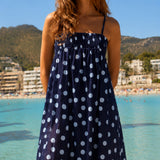 Woman in a polka dot dress standing by a beach with mountains in the background