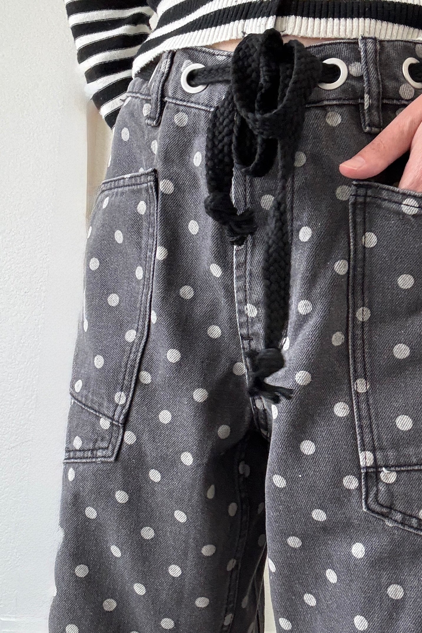 Close-up front detail of Moxie Barrel Eyelet Jeans in Polka Dot Black featuring eyelet waist detail, corded drawstring, and polka dot denim.