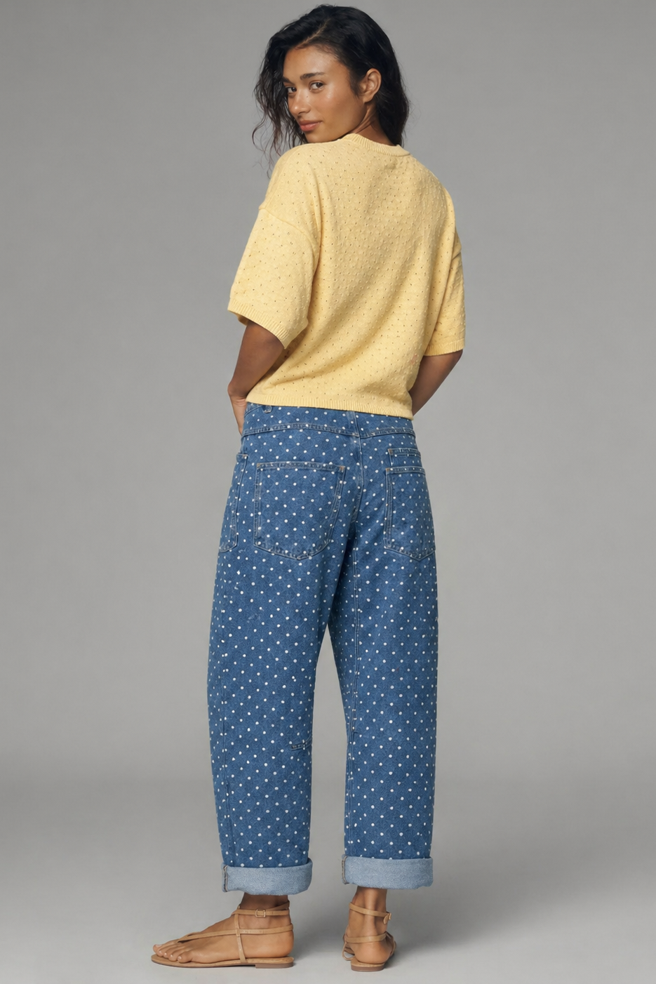 Woman wearing a yellow top and blue patterned pants on a gray background