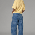 Woman wearing a yellow top and blue patterned pants on a gray background
