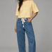 Woman wearing Moxie Polka Dot Barrel Jeans in Denim and yellow top styled in a full outfit on a gray background