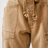 Close-up detail of waist eyelet design and drawstrings on the rust jeans
