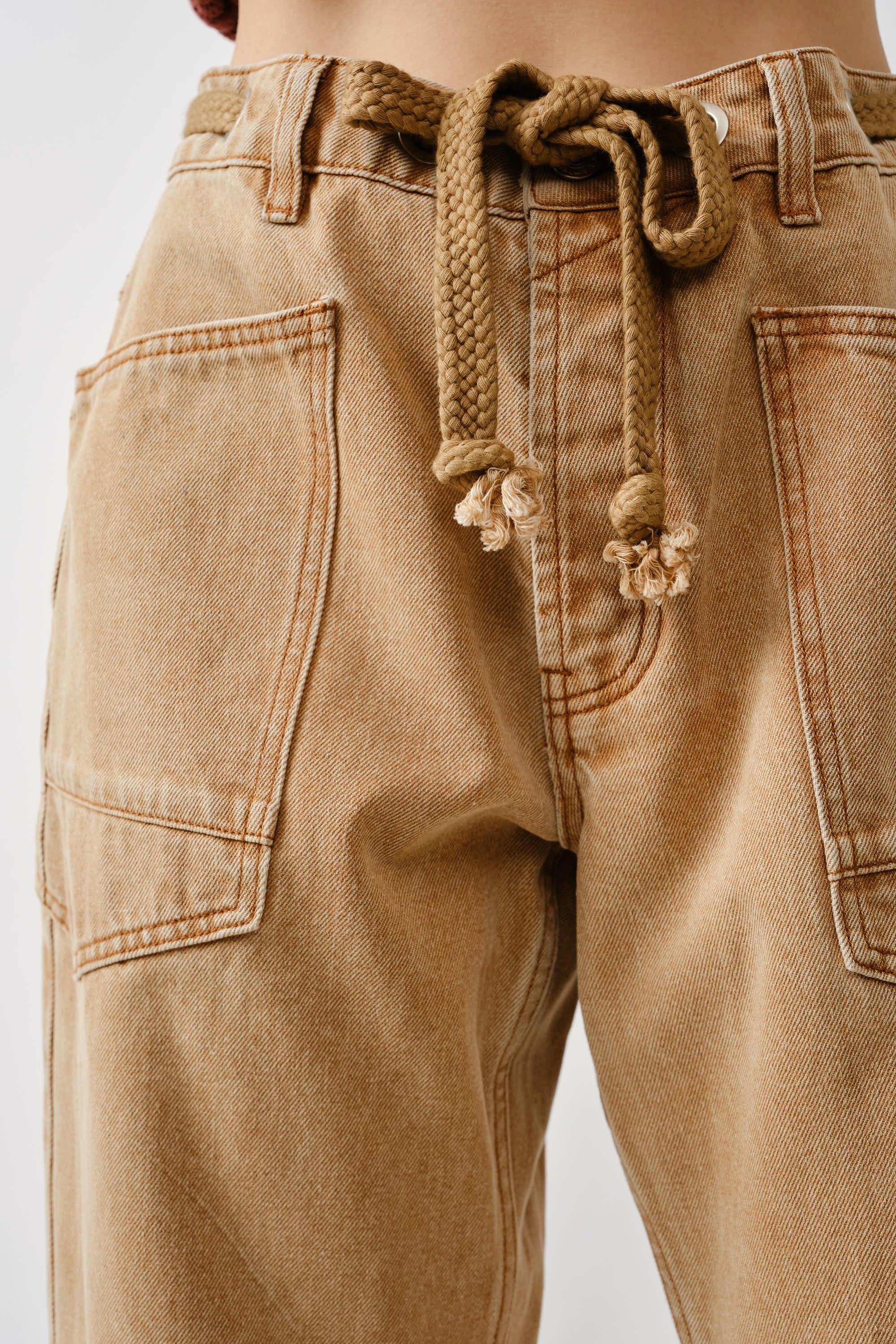 Close-up detail of waist eyelet design and drawstrings on the rust jeans