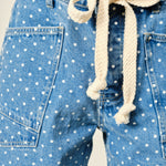 Close-up of Moxie Barrel Shorts in Denim Dot showing the drawstring waist, eyelet detail, polka dot denim, and front snap closure.