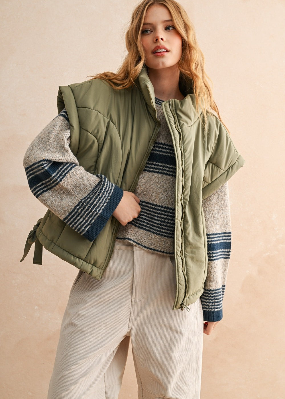 Woman wearing an olive green puffer vest with quilted texture over striped sweater and beige pants — cozy women’s outerwear for fall layering.