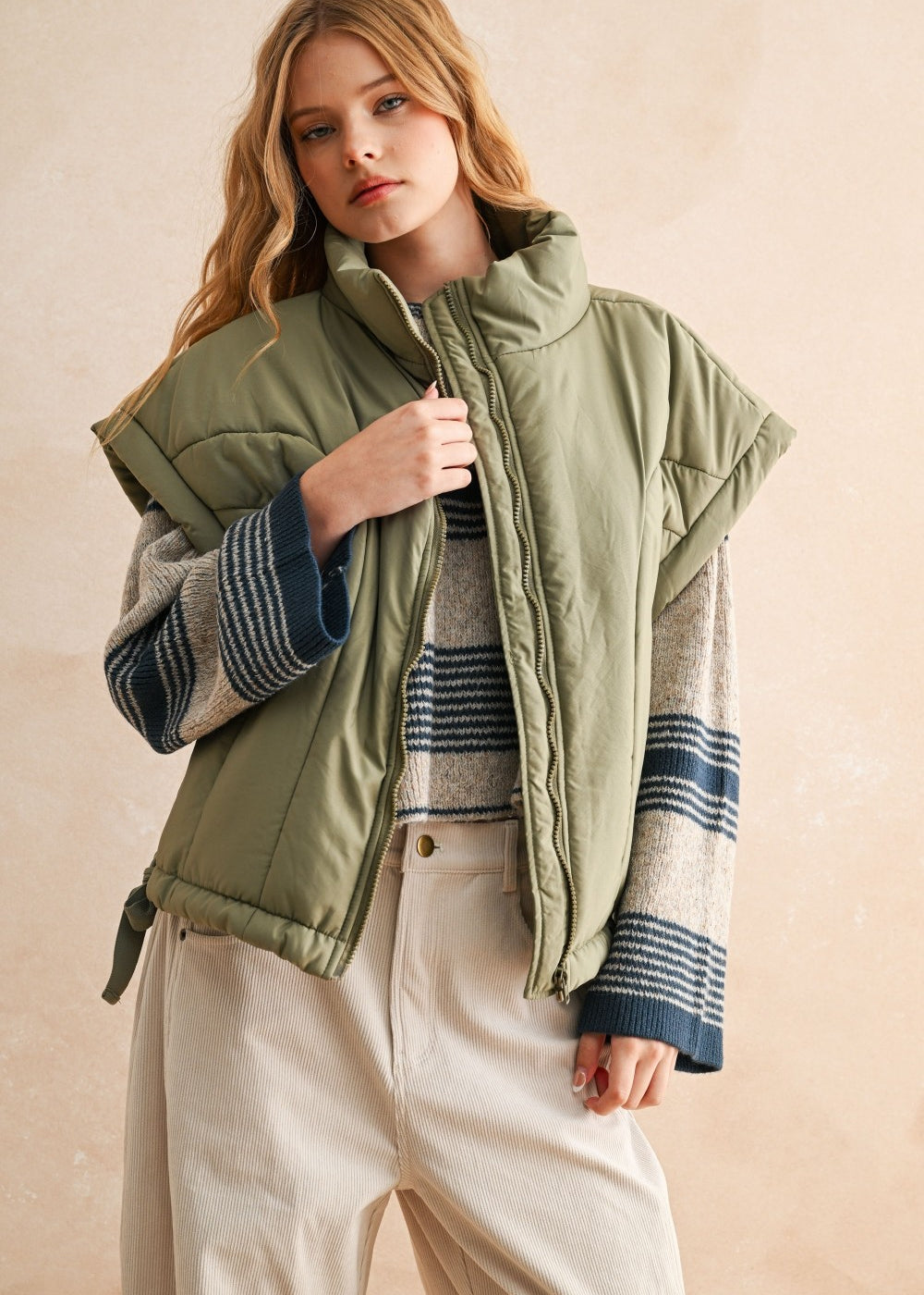 Olive green puffer vest styled with striped knit and cream pants — modern women’s layering piece for cool weather.