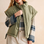 Olive green puffer vest styled with striped knit and cream pants — modern women’s layering piece for cool weather.