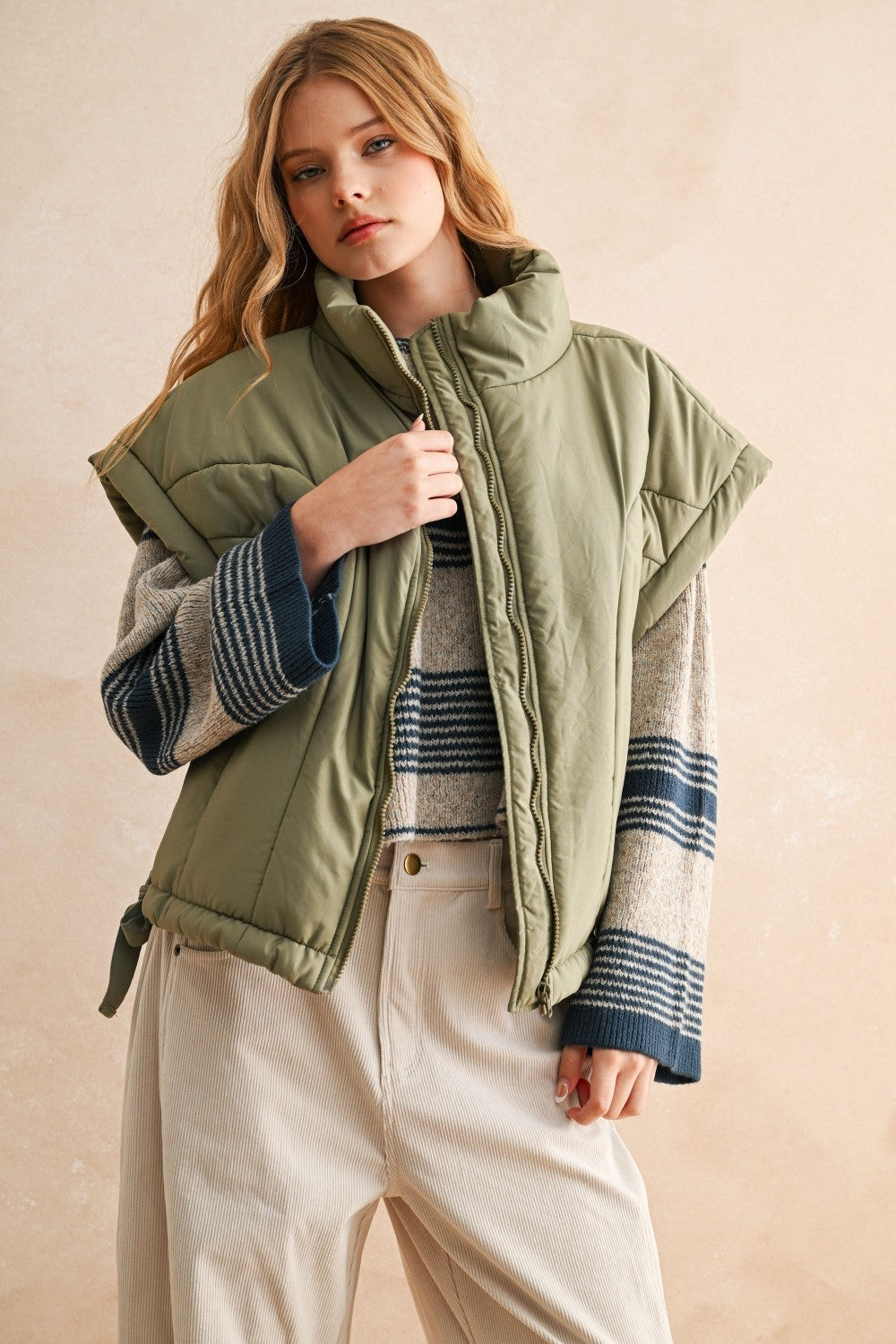 Olive green puffer vest styled with striped knit and cream pants — modern women’s layering piece for cool weather.