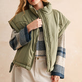 Olive green puffer vest styled with striped knit and cream pants — modern women’s layering piece for cool weather.