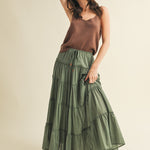 Woman wearing a brown top and green tiered skirt on a beige background