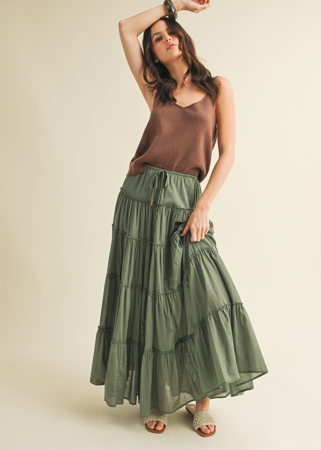 Woman wearing a brown top and green tiered skirt on a beige background