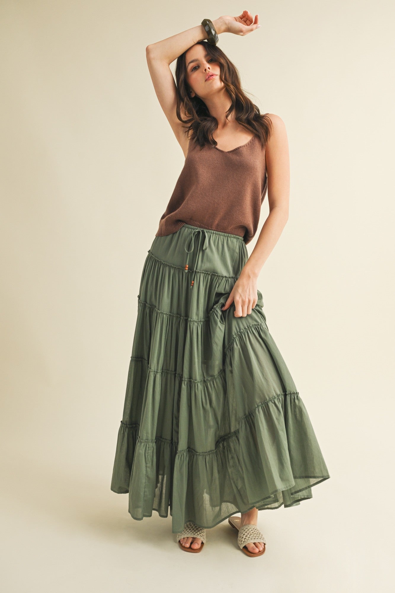 Woman wearing a brown top and green tiered skirt on a beige background