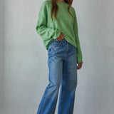 Model wearing the Piper Soft Knit Crew Sweater in Green with relaxed neutral pants - side view