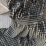 Close-up video of black and white gingham smocked jumpsuit showing cotton fabric texture and open-back strap detail