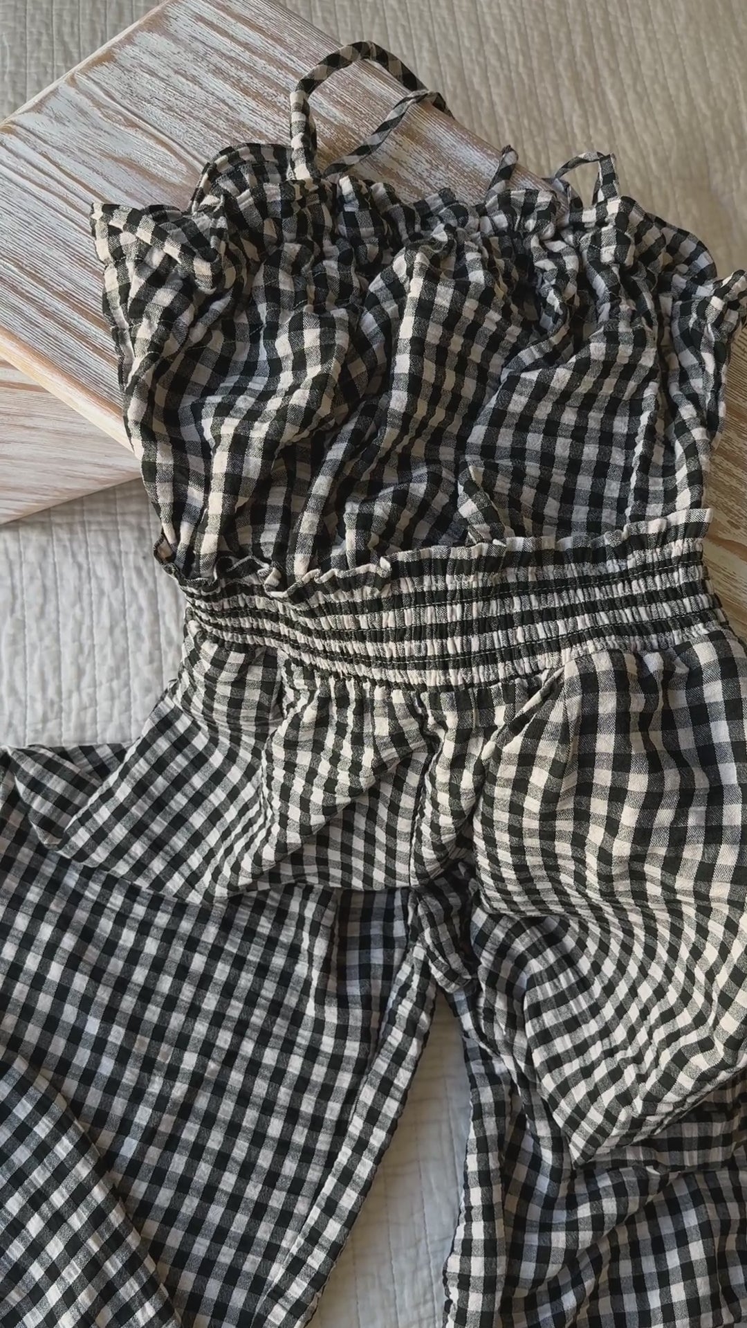 Close-up video of black and white gingham smocked jumpsuit showing cotton fabric texture and open-back strap detail