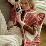Lifestyle photo of model sitting on a couch wearing the red gingham sherpa puffer vest layered over a long sleeve top