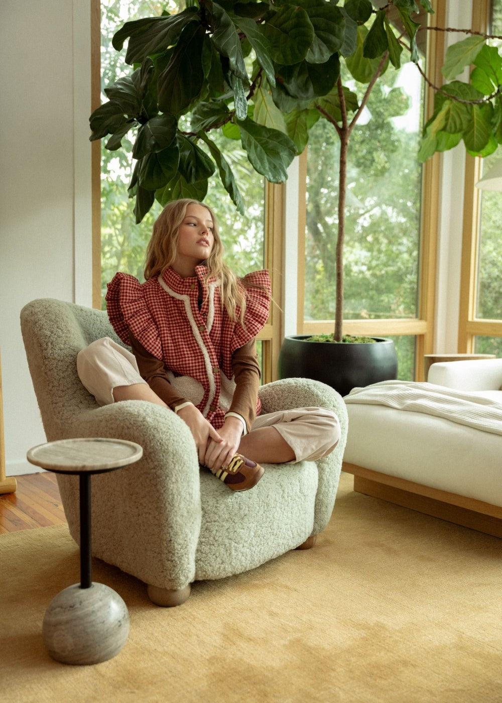 lifestyle view of model in the red gingham sherpa puffer vest sitting in a chair, full outfit visible