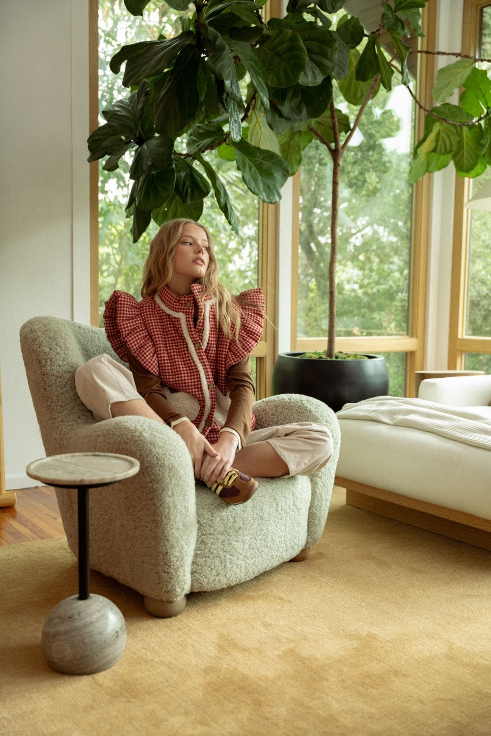 lifestyle view of model in the red gingham sherpa puffer vest sitting in a chair, full outfit visible