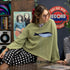 Lifestyle image of model wearing the Sardine Balloon Sleeve Sweater in olive inside a record store