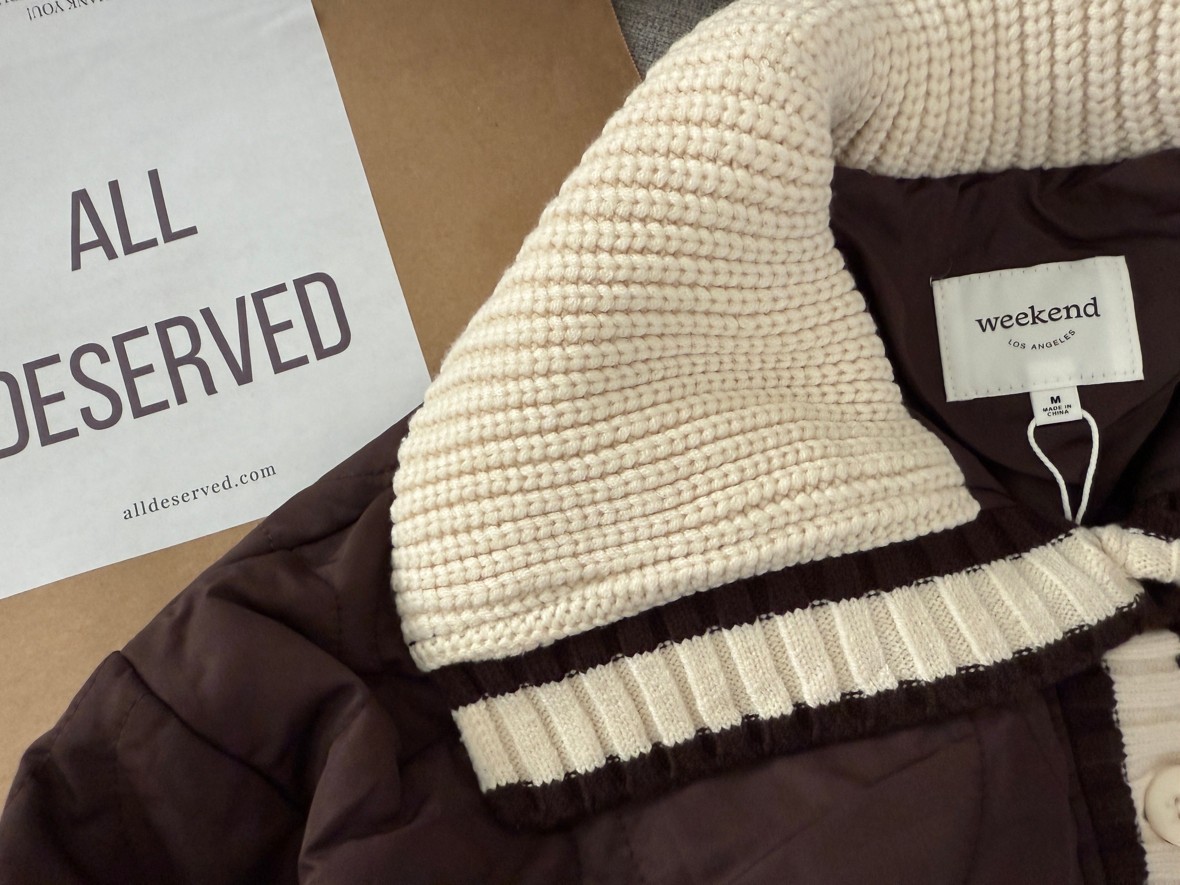 Close-up of the All Deserved label and knit collar trim on the brown puffer jacket