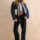 Full-body view of the blue quilted jacket with sherpa pockets styled with black pants and a beanie