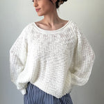 Woman wearing a white knitted sweater and blue striped pants against a plain background