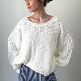 Woman wearing a white knitted sweater and blue striped pants against a plain background