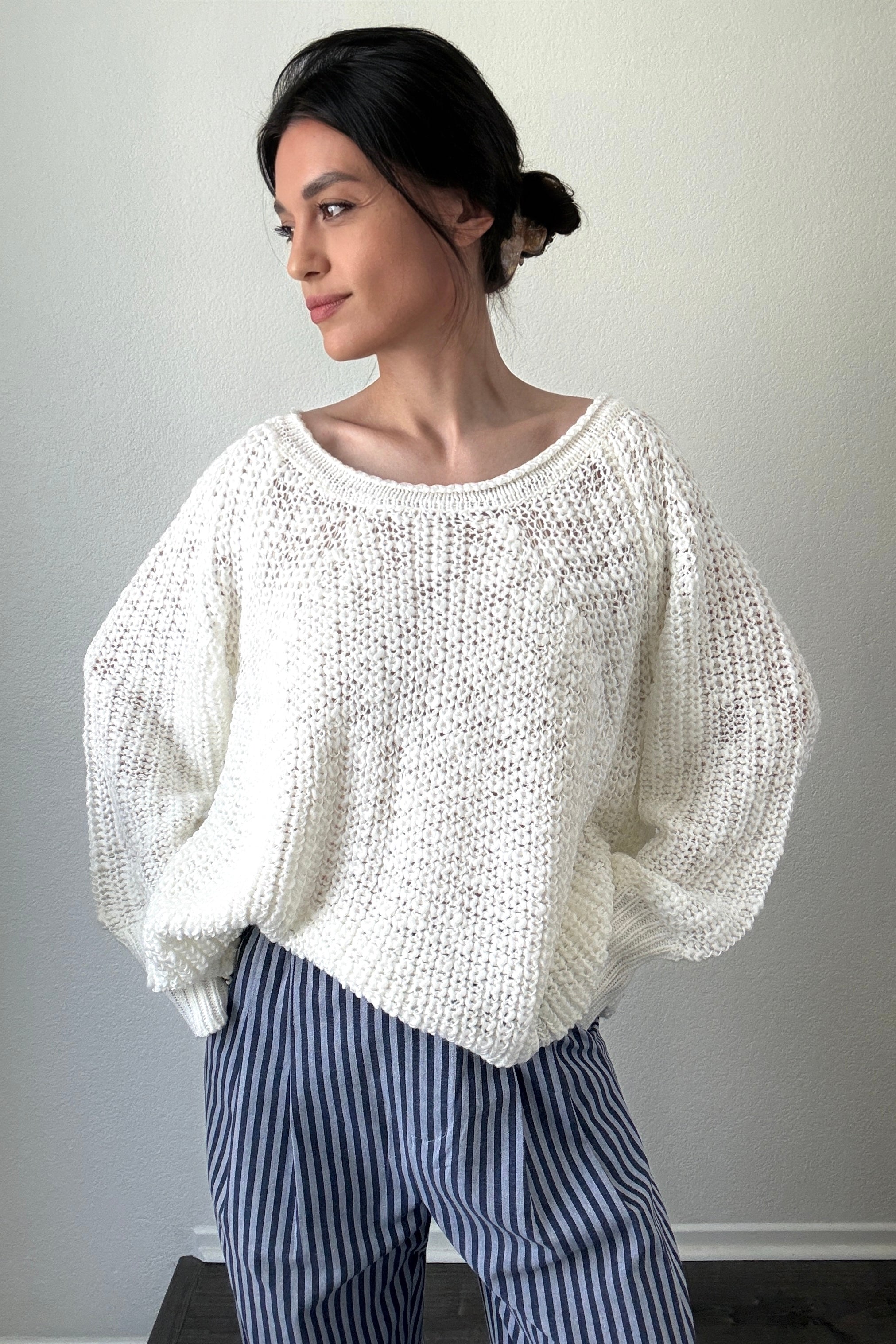 Woman wearing a white knitted sweater and blue striped pants against a plain background