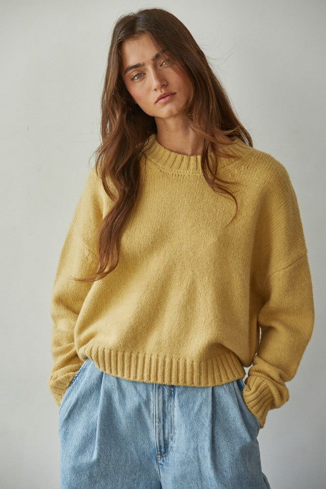 Woman wearing a honey yellow sweater and blue jeans against a plain background