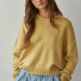 Woman wearing a honey yellow sweater and blue jeans against a plain background