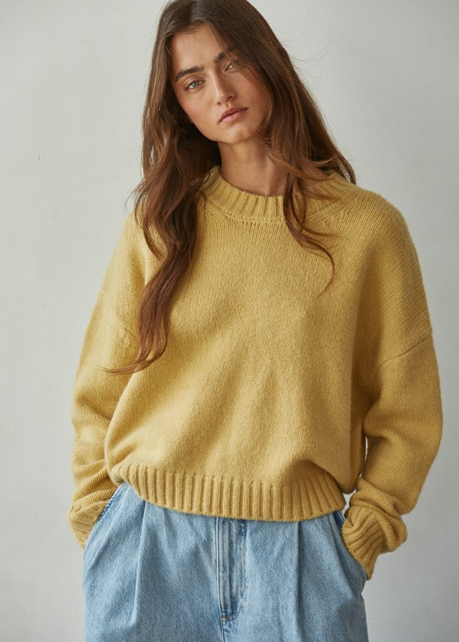 Woman wearing a honey yellow sweater and blue jeans against a plain background