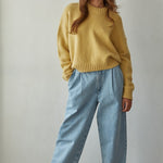 Woman wearing a honey sweater and light blue jeans against a plain background