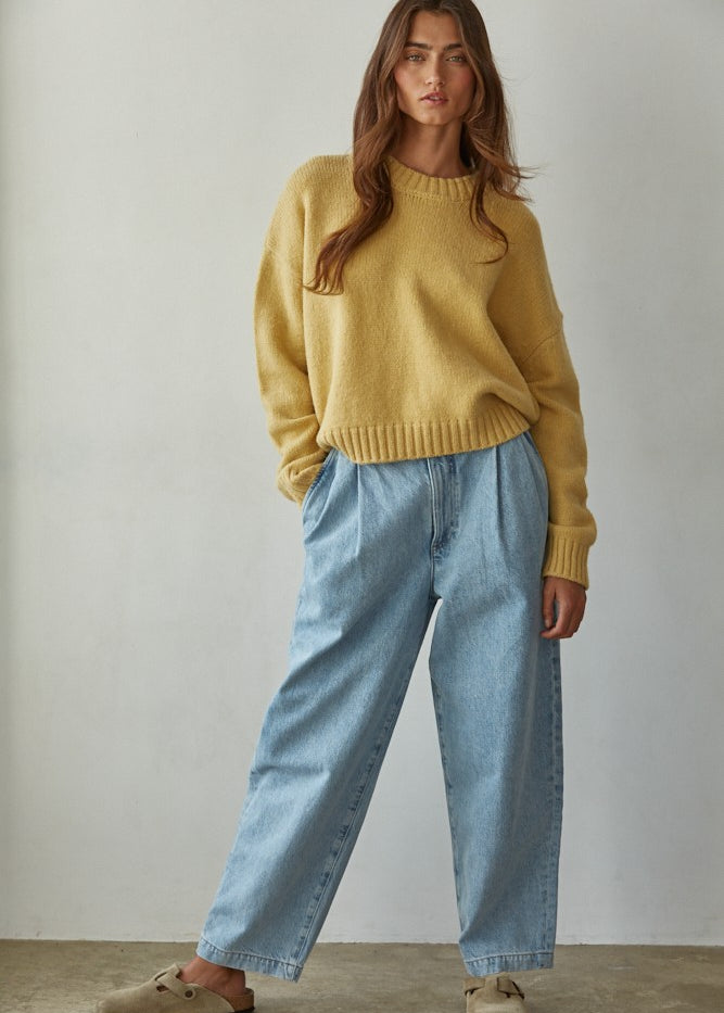 Woman wearing a honey sweater and light blue jeans against a plain background