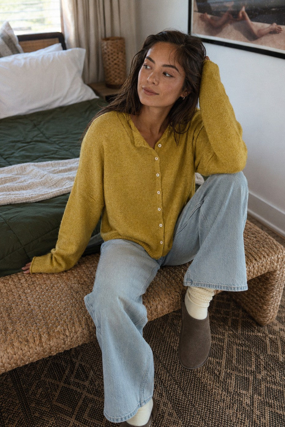 Woman wearing the Things Between Piper Cardigan in Dijon Yellow in a relaxed seated lifestyle setting