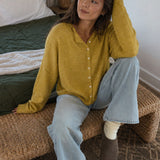 Woman wearing the Things Between Piper Cardigan in Dijon Yellow in a relaxed seated lifestyle setting