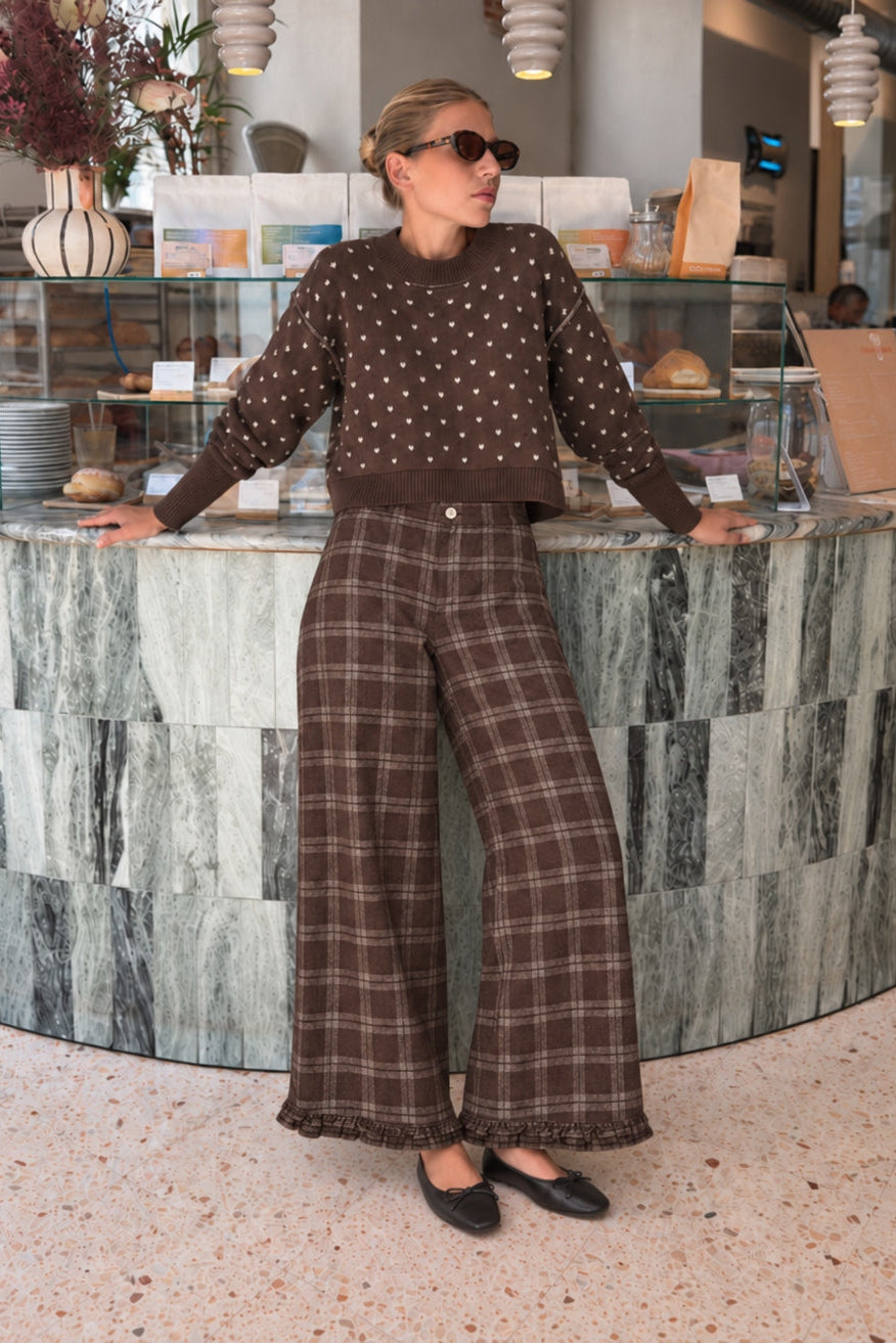 Woman wearing Trudy chocolate plaid wide-leg pants inside a coffee shop