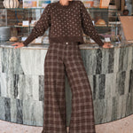 Woman wearing Trudy chocolate plaid wide-leg pants inside a coffee shop