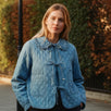 Woman wearing Chloe Bow Quilted Denim Jacket in denim with quilted texture, bow tie closure, and lace Peter Pan collar