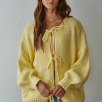 Woman wearing a yellow knitted bow tie cardigan against a plain background