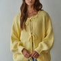 Woman wearing a yellow knitted bow tie cardigan against a plain background
