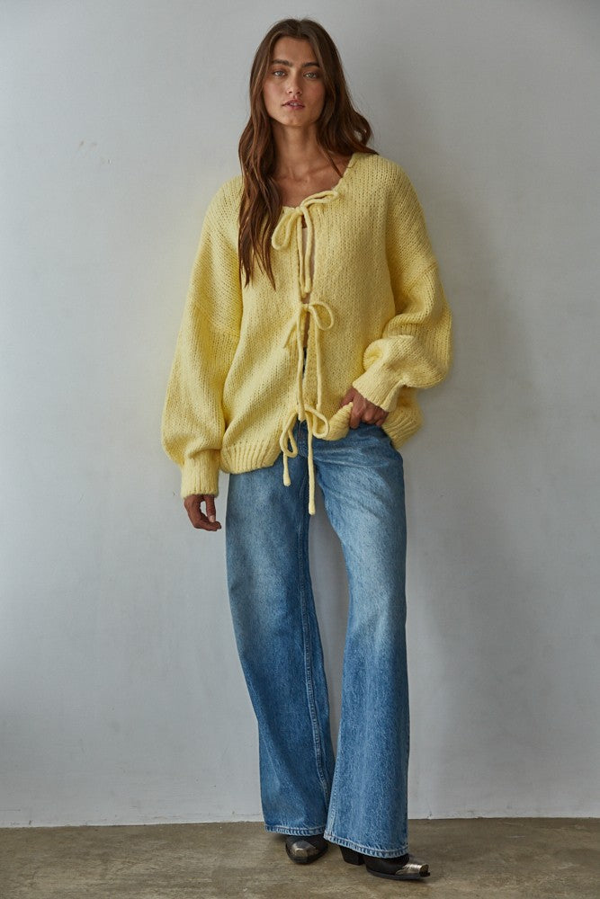 Woman wearing a yellow bow tie cardigan  and blue jeans against a plain background