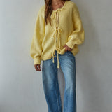 Woman wearing a yellow bow tie cardigan  and blue jeans against a plain background